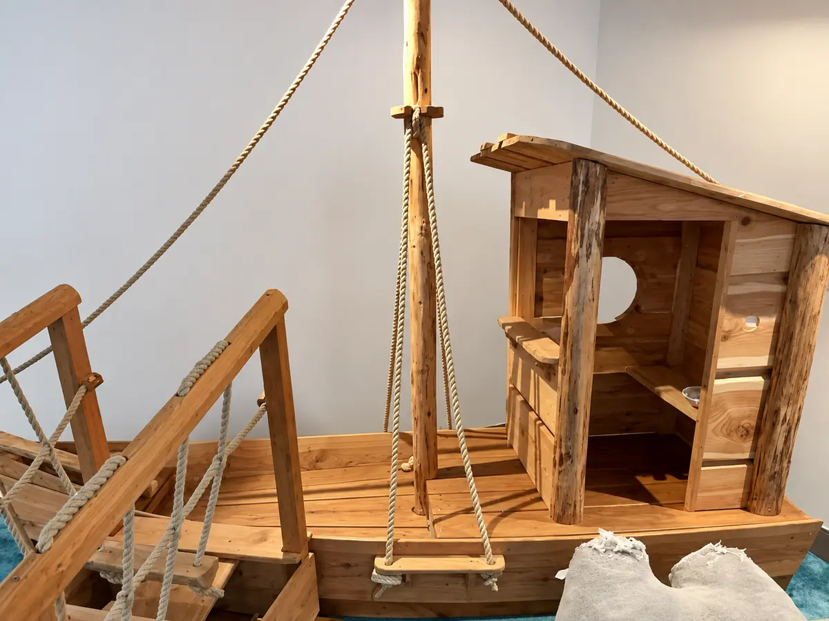 Großes Holzboot mit Brücke, Seilen und kleiner Kabine im Spielbereich des Café Nebenan in Emden